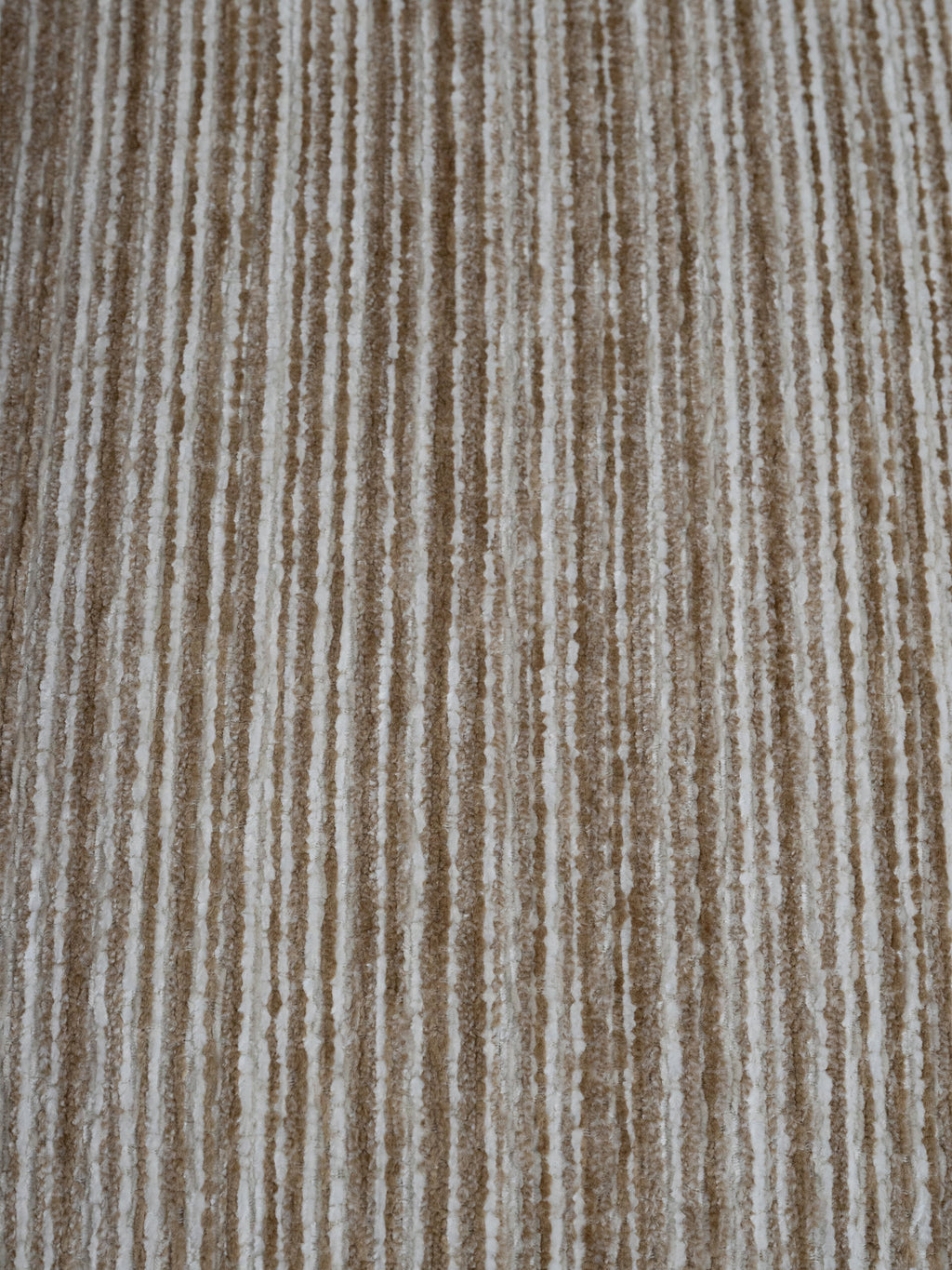 A close-up of a textured fabric or carpet with vertical stripes in warm beige, tan, and off-white.