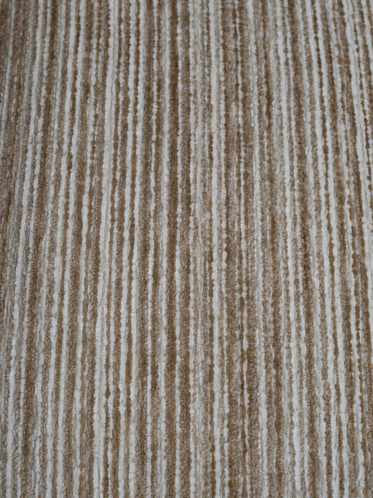 A close-up of a textured fabric or carpet with vertical stripes in warm beige, tan, and off-white.