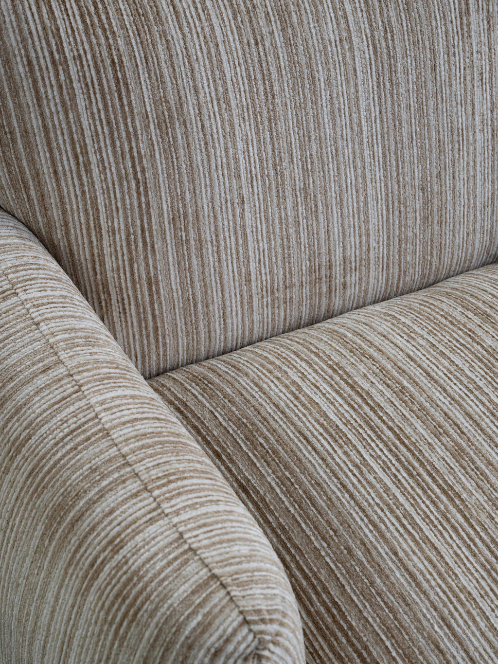 Close-up of a textured fabric armchair with vertical ribbed upholstery in warm taupe and beige tones.