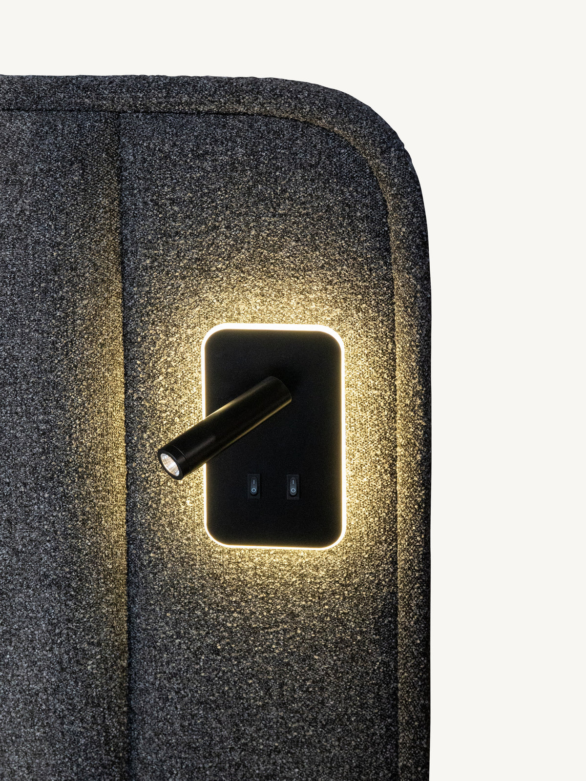 Close-up of a dark gray textured fabric surface with a built-in black rectangular light panel emitting warm yellow light, showing a small adjustable light bulb.