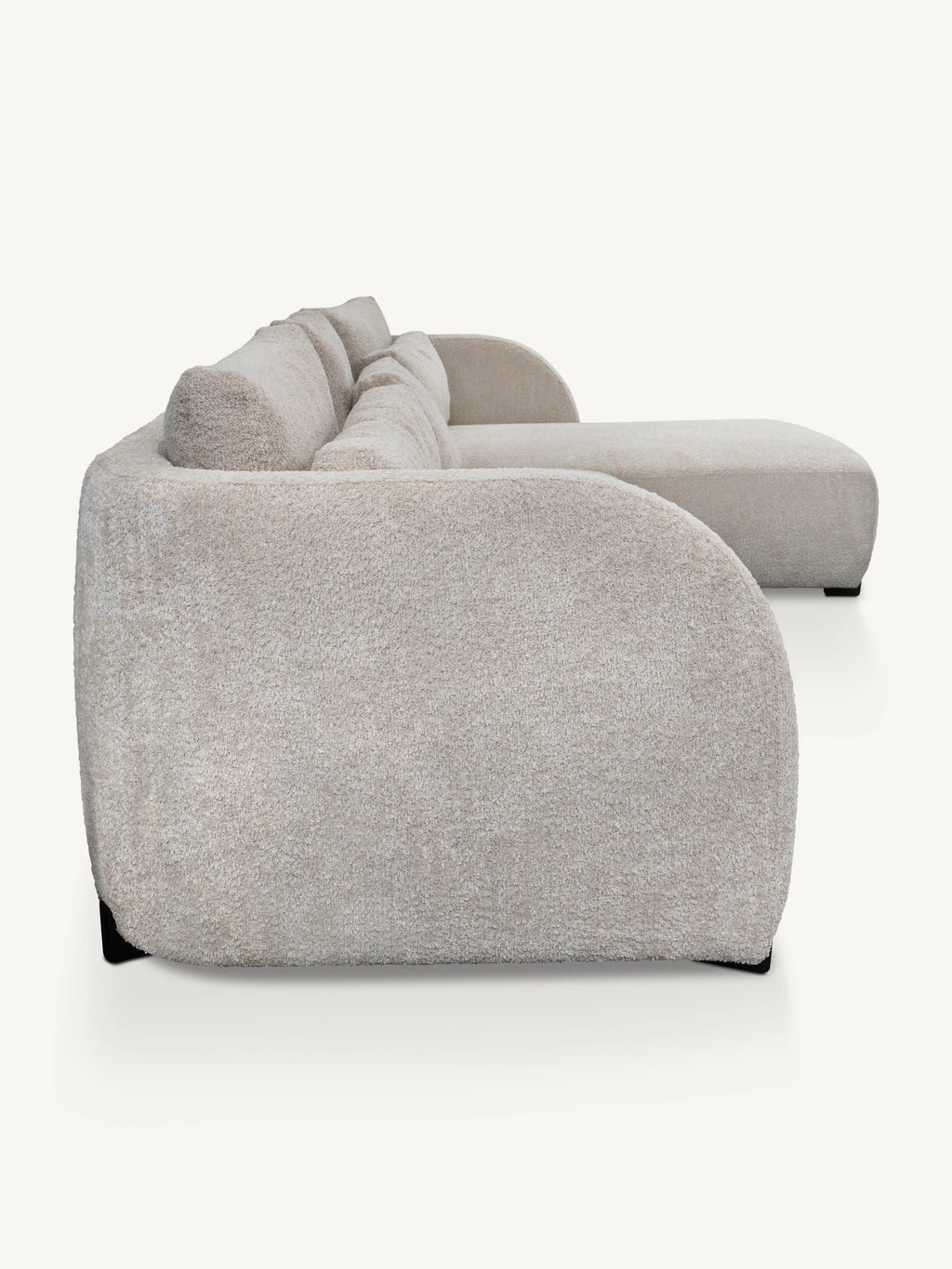 A modern curved sofa upholstered in a textured light beige bouclé fabric, shown from a side angle against a clean off-white background.
