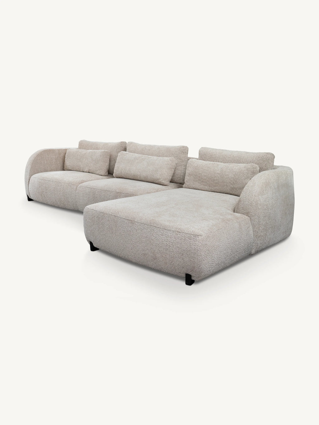 A modern modular sectional sofa upholstered in a textured light beige fabric, featuring a chaise lounge on the front right and multiple matching back cushions, shown against a plain off-white background.