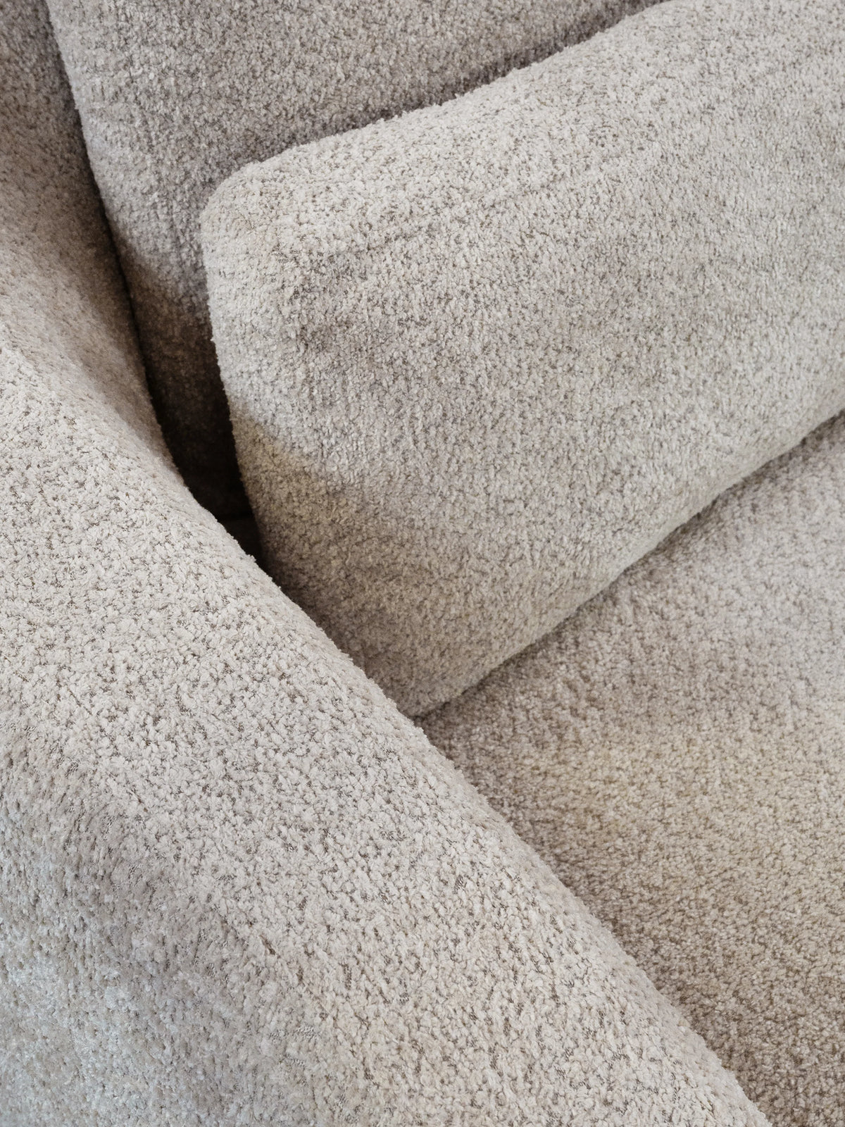 Close-up of a textured bouclé fabric sofa cushion in a warm light beige color.