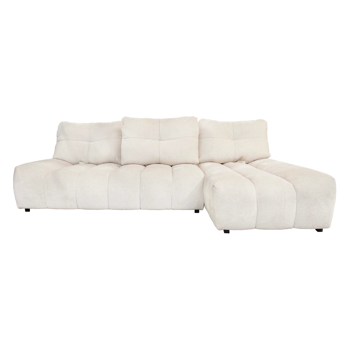 A modern modular sectional sofa upholstered in a soft, textured cream fabric, featuring a low-profile design with tufted square cushions and a right-facing chaise lounge.