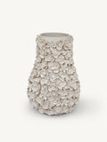 A textured ceramic vase with a flared rim, covered in raised 3D floral rose motifs, in a warm off-white/cream color, set against a solid light gray background.