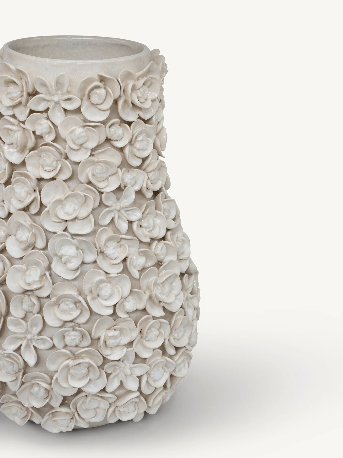 A textured ceramic vase covered in sculpted 3D flowers, shown on a clean off-white background.