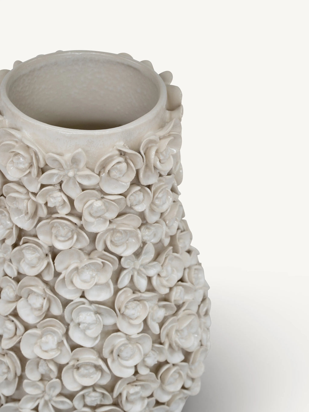 A close-up of a textured ceramic vase with a dense, 3D floral relief pattern in a warm off-white or cream glaze, set against a plain light background.