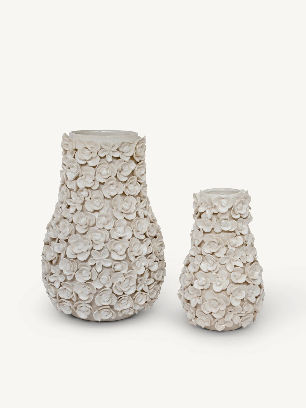 Two textured ceramic vases with a raised floral pattern, one larger and one smaller, in a warm off-white/cream color on a light gray background.
