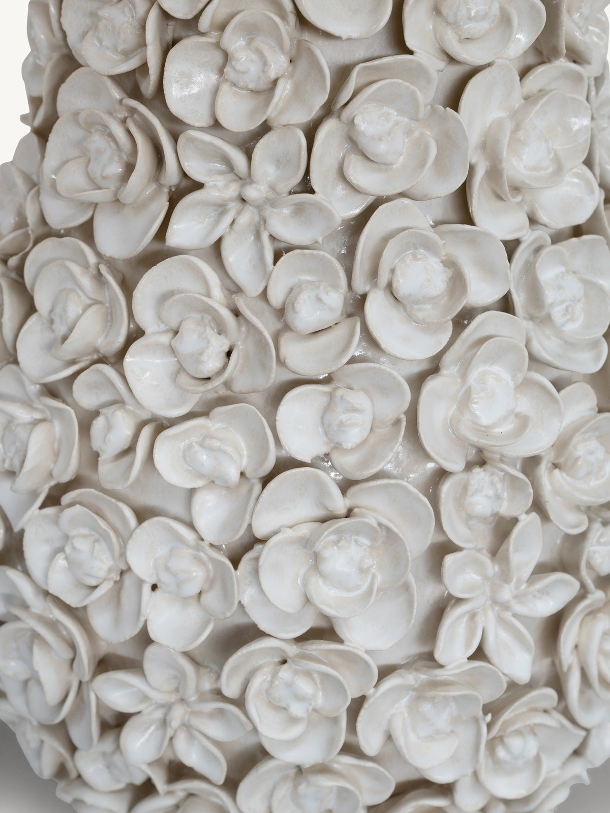 Close-up of a glossy white ceramic vase covered in sculpted floral motifs, including roses, lilies, and small blossoms.
