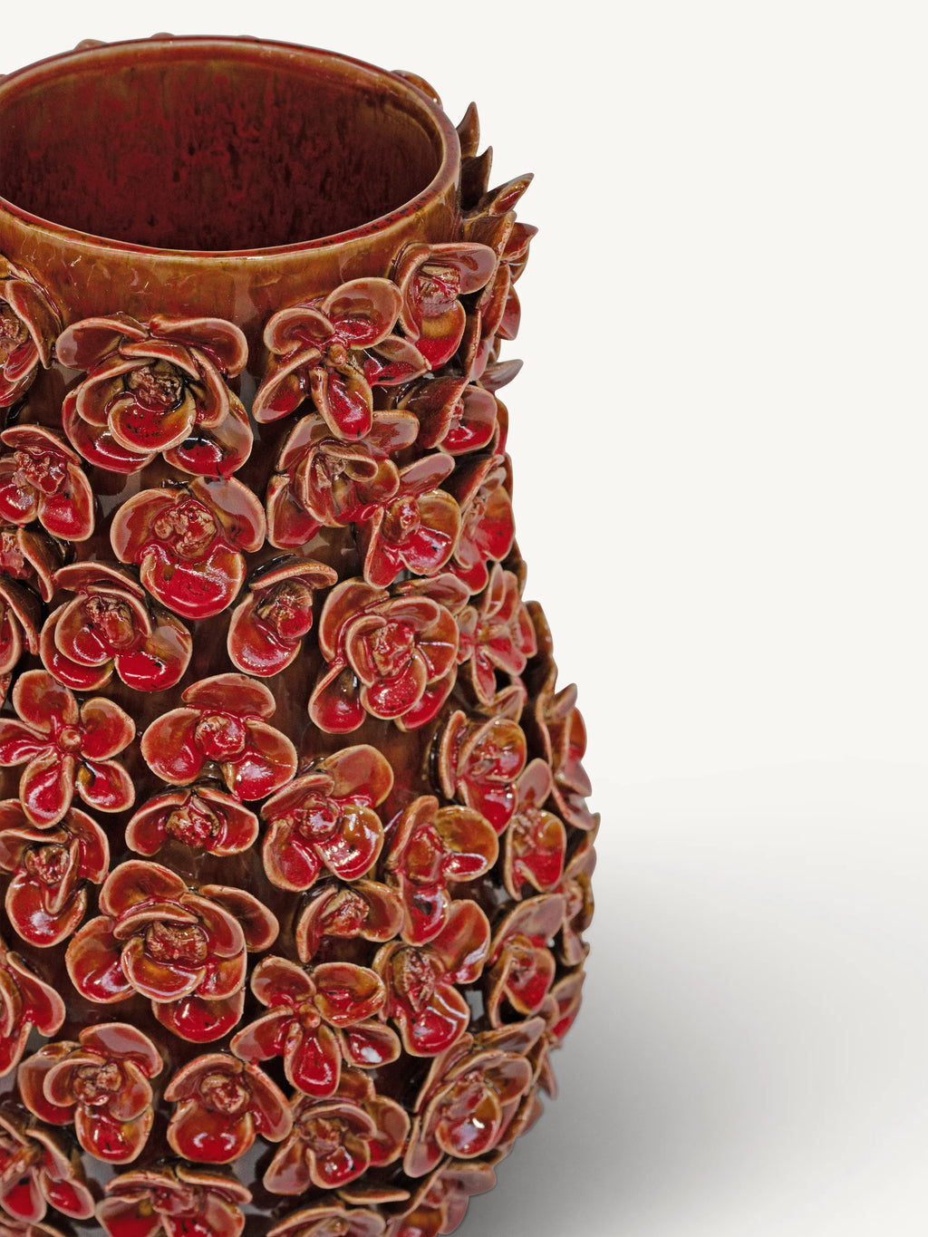 A close-up of a glossy ceramic vase covered in sculpted orchid flowers in reddish-brown and deep red glaze, set against a plain light gray background.