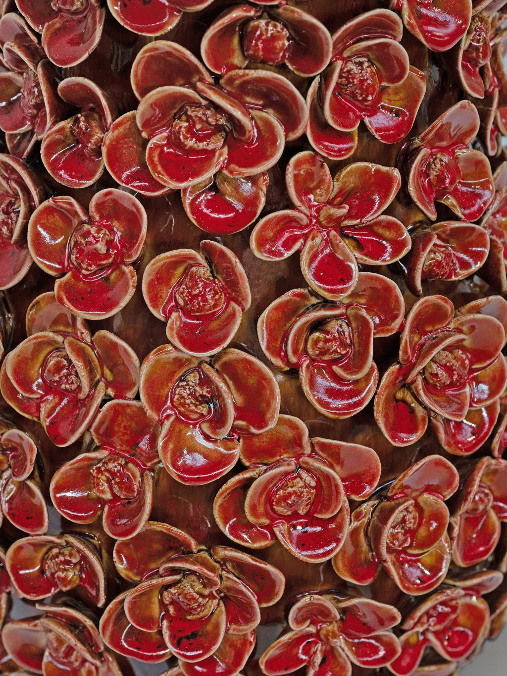 A close-up of a glossy floral pattern featuring repeating red and brown flower-like motifs with a shiny glazed finish.