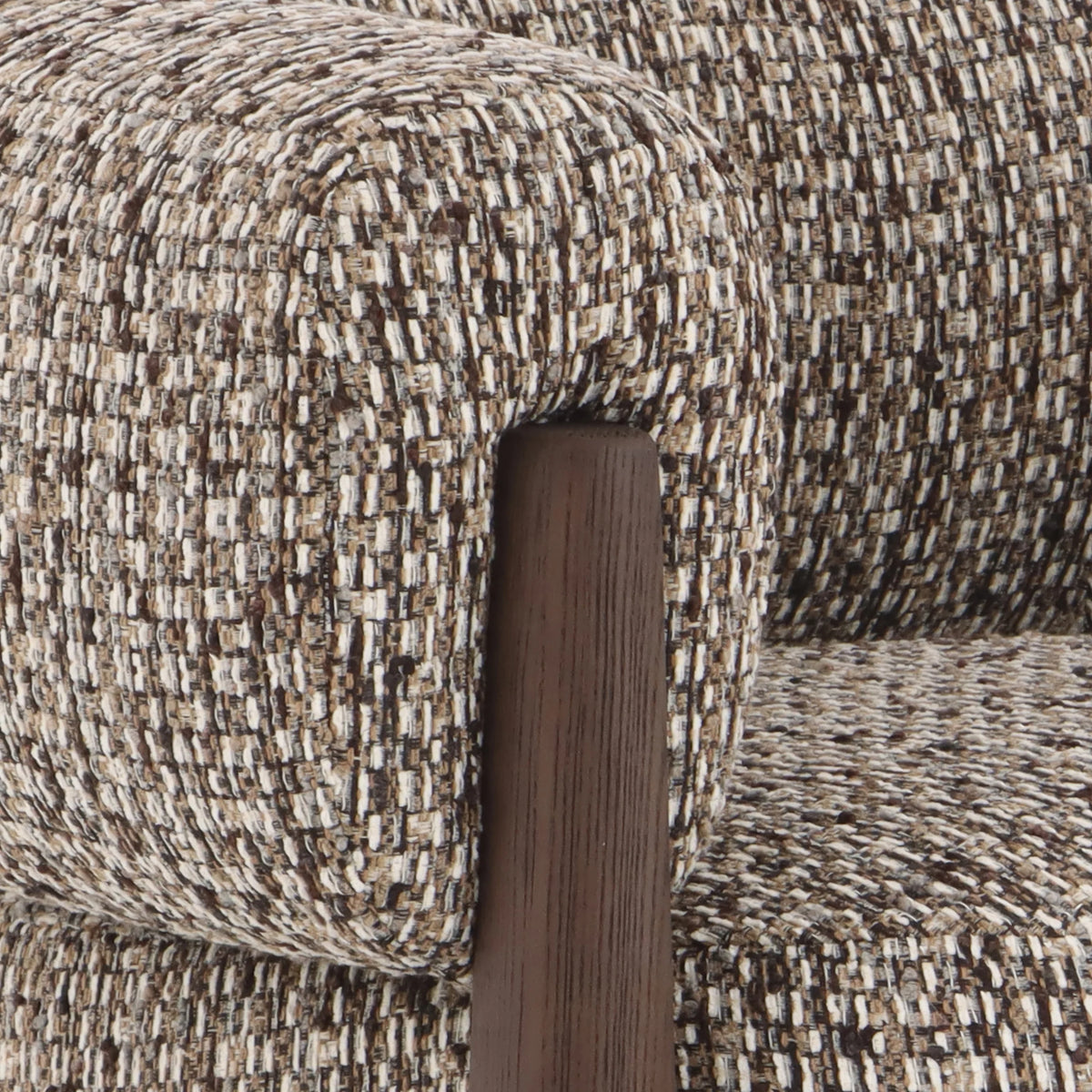 Close-up of a textured woven upholstery fabric in beige, brown, and cream tones, with a dark brown wooden armrest visible.